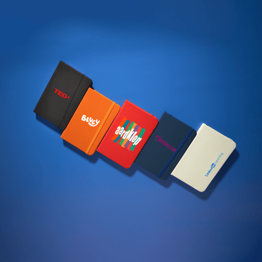 A collection of five Minichroma A6 Notebooks in various colours: red, orange, blue, navy, and white, each featuring a logo.