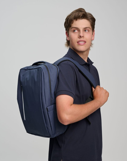A navy blue backpack is worn over one shoulder by a young man in a navy polo shirt. The backpack features a logo.