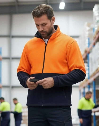A Hi-Vis polar fleece full zip jacket in bright orange and navy, worn by a man using a phone.