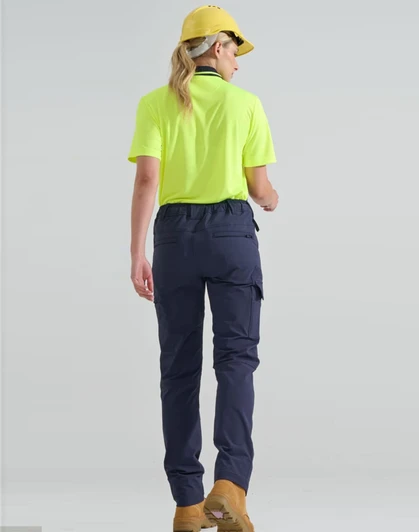 A woman wearing a bright yellow shirt and navy flexi work pants, seen from the back, with a cap and boots.
