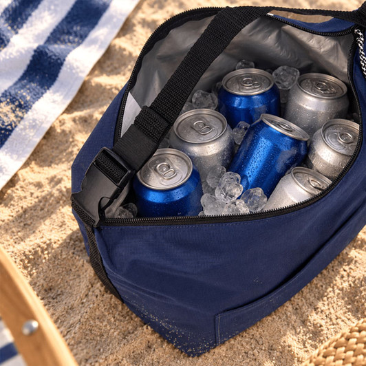 A navy cooler bag filled with ice and assorted cans, placed on sandy ground alongside a beach towel.