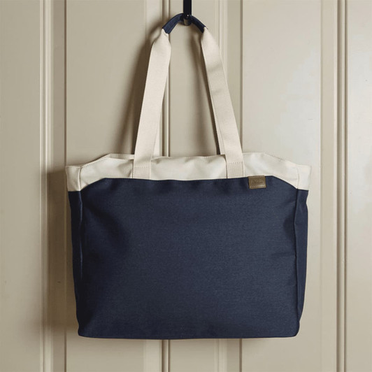 A navy blue tote bag with cream handles, featuring a logo on the front, hanging against a wall.