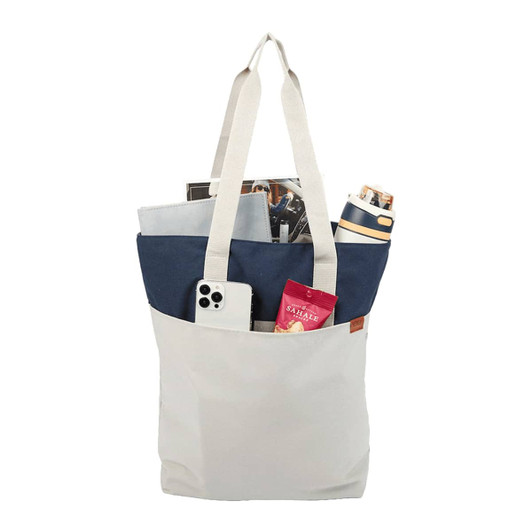 A white and navy tote bag with a drink bottle, phone, magazines, and a snack pack visible inside.