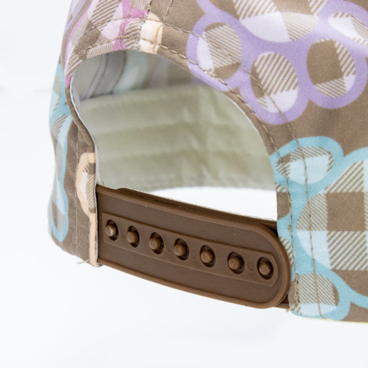 A cap featuring a colourful patterned fabric and an adjustable brown strap at the back, along with a logo.