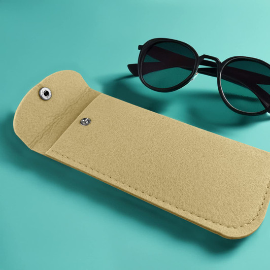 A yellow felt pouch lies on a teal surface next to a pair of black sunglasses, featuring a snap closure.