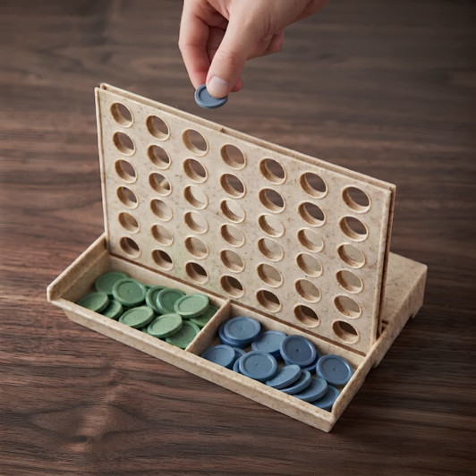 A hand placing a token into a wooden Connect Four game with green and blue tokens stored below.