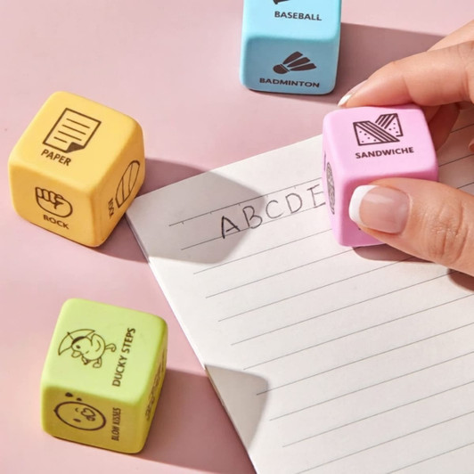 A collection of coloured cubes in yellow, pink, and blue, with various illustrations, next to a lined notepad.