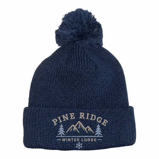 A navy knitted beanie with a pom pom on top and a logo featuring mountains and text.