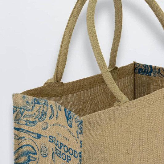 A jute tote bag featuring a natural beige colour with a blue design and sturdy handles. It has branding on the side.