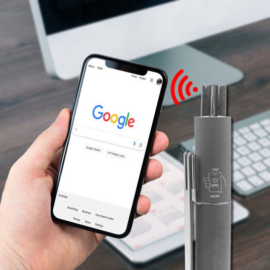 A grey metal pen with an NFC feature, placed beside a smartphone displaying a web search.