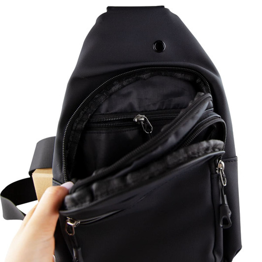 A black sling bag is shown, featuring multiple zippered pockets and a hand holding it open to display the interior.