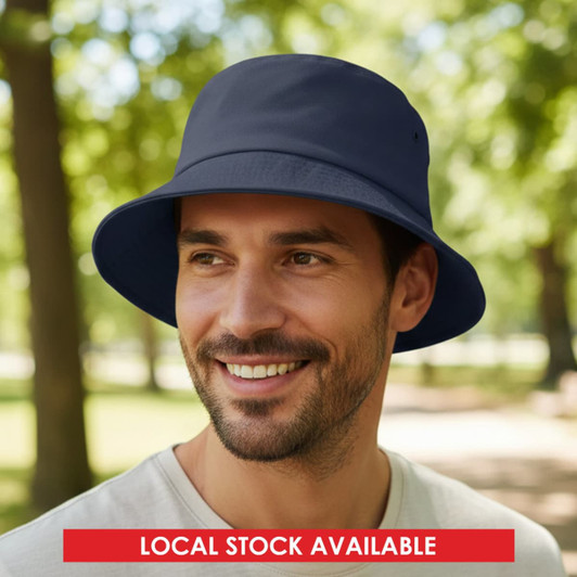 A navy blue bucket hat displayed on a smiling man, set against a park backdrop with trees. The hat has a logo.