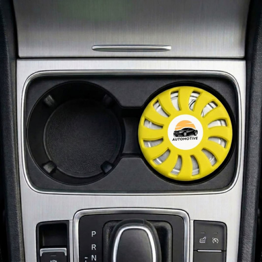 A round, yellow air freshener is placed in a car cup holder, featuring a logo and a vented design.