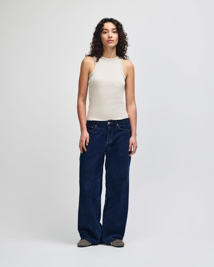 A fitted tank in beige worn with wide-leg denim jeans, featuring a model against a plain background.