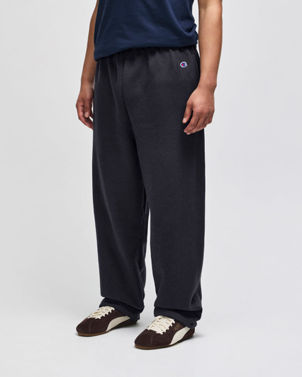 Open-bottom fleece pants in dark grey featuring pockets and a logo, worn by a person standing.
