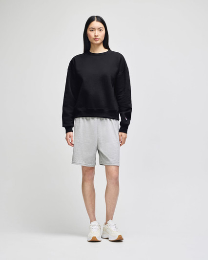 A black crewneck sweatshirt worn with grey shorts, paired with white sneakers, featuring branding.
