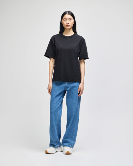 A black Champion Adult Heritage Jersey T-shirt displayed on a model wearing blue jeans and white sneakers.