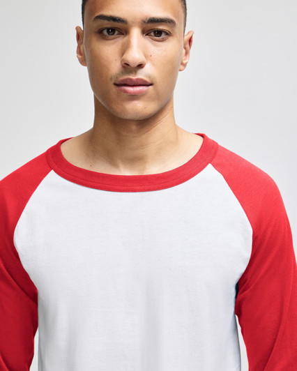 A model wearing a white and red raglan baseball T-shirt with three-quarter sleeves, paired with dark pants.