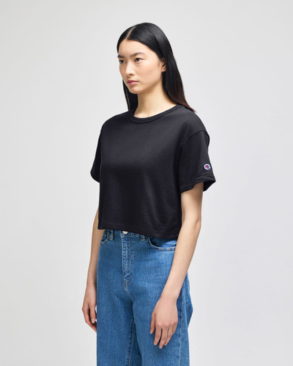 A cropped black t-shirt with short sleeves and a logo detail, styled with blue denim jeans.