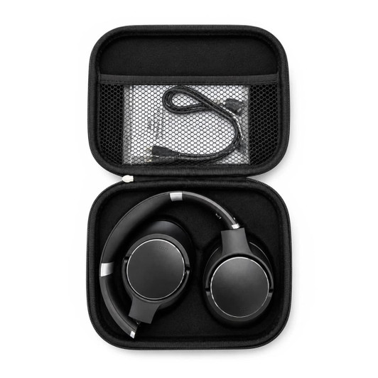 A pair of black wireless headphones packed in a compact black carrying case, with a charging cable inside.