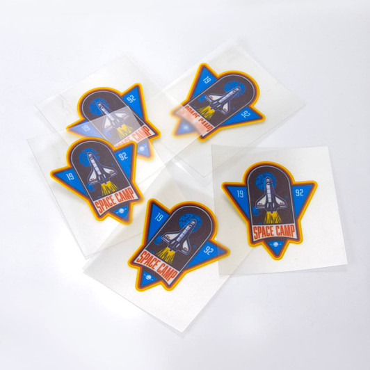 A collection of five 50 x 50mm stickers featuring a rocket and 'Space Camp' design, with vibrant blue, orange, and white colours.