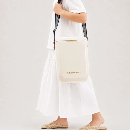 A cream cooler bag carried over the shoulder, featuring a branding logo and set against a neutral background.