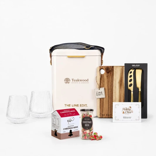 A festive gift set featuring two glass tumblers, a wine cooler, a wooden board, a knife, and Christmas-themed treats.