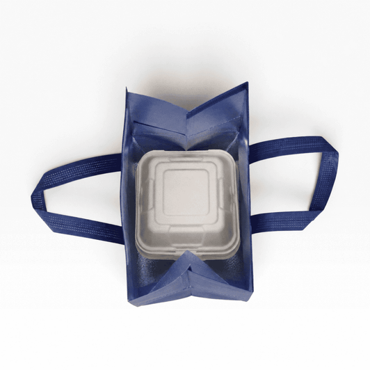 A navy insulated reusable bag with two handles, containing a square white food container inside. It has a logo on the exterior.