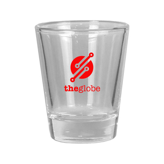A clear glass shot glass with a solid base and a round logo in red and white.