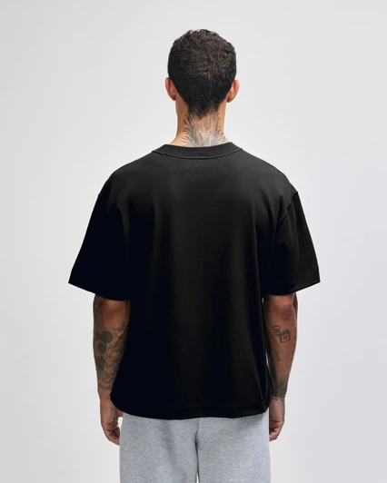 A black heavyweight cotton unisex boxy T-shirt displayed from the back, worn over grey shorts.