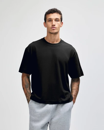 A black heavyweight cotton unisex boxy t-shirt worn by a model, paired with grey sweatpants.