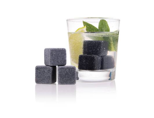 A drink glass with mint and lime contains grey gin stones beside it, set against a white background.