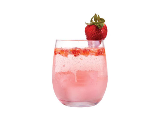 A glass of pink strawberry drink with ice and fresh strawberries on top, served in a clear tumbler.