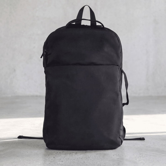 A black backpack with a sleek design and a front pocket, featuring straps and a logo on the side.