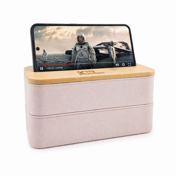 A pink eco lunch box with a bamboo lid featuring a phone holder, displaying a video on a smartphone.