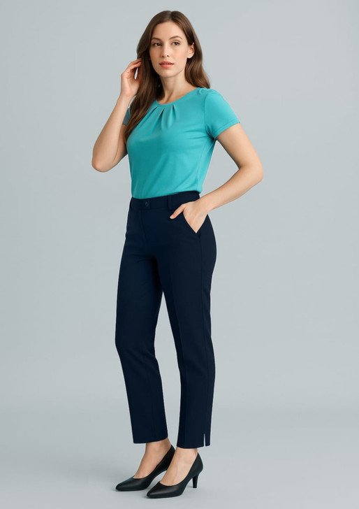 A woman in a turquoise top and navy slim leg pants stands against a neutral background. The pants feature pockets and a logo.