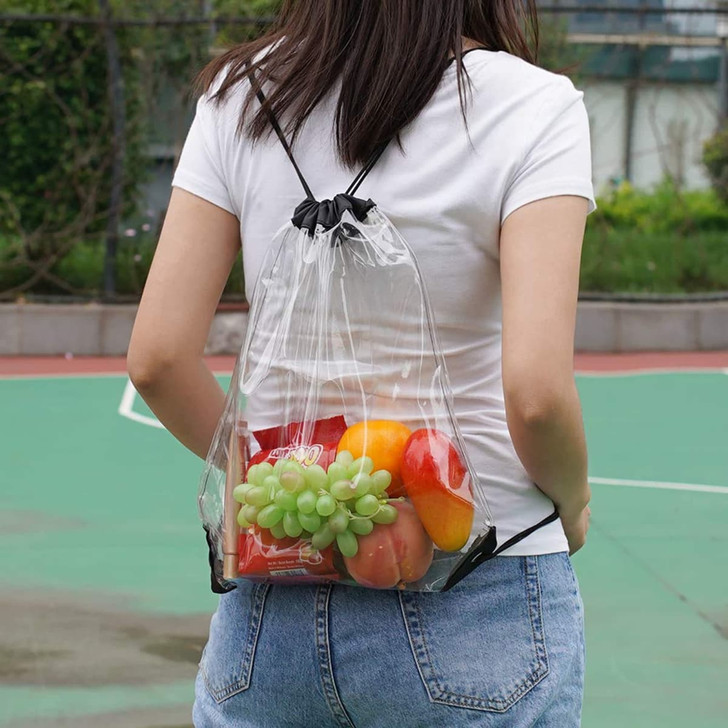 A transparent drawstring backpack filled with assorted fruits, held by a person wearing a white shirt and denim shorts.
