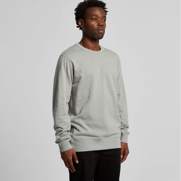 A model wearing a light grey crew jumper, featuring a simple design and long sleeves. The jumper has a logo.