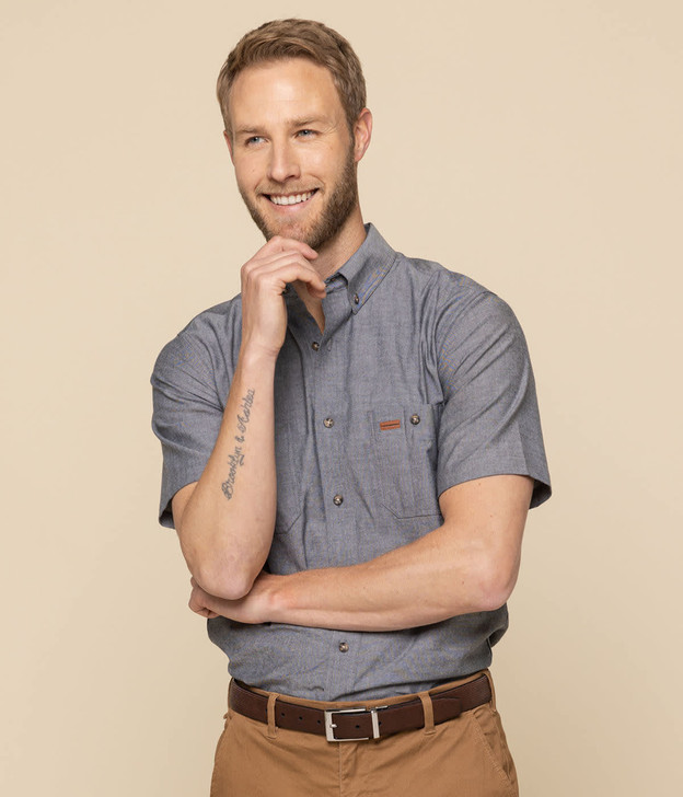 A short-sleeved grey work shirt with a collar and a logo, worn by a smiling man with light hair.