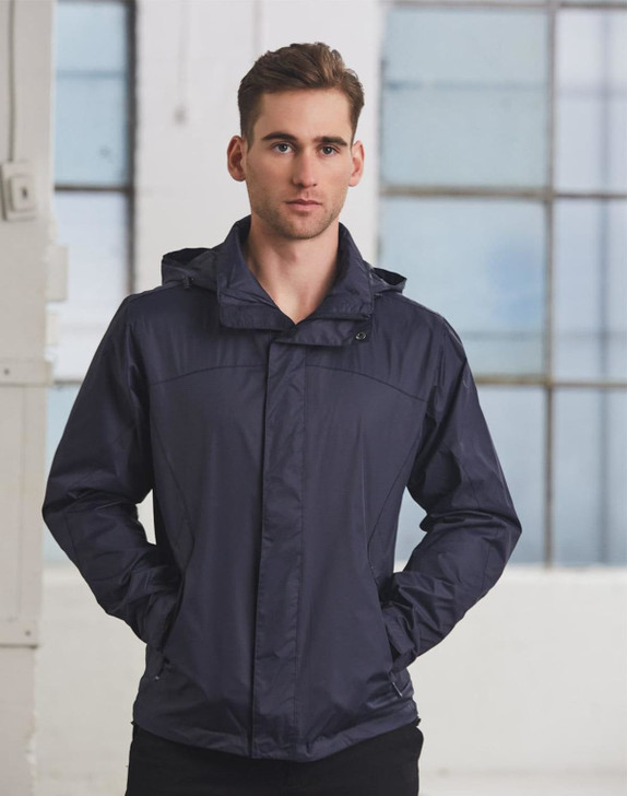 A man wearing a navy versatile jacket, standing with hands in pockets against a backdrop of large windows.