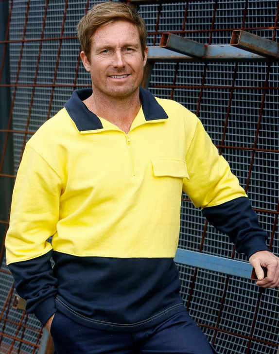 A man wearing a hi-vis two-tone yellow and navy cotton fleecy sweatshirt with a zip and pocket, posed against a metal backdrop.