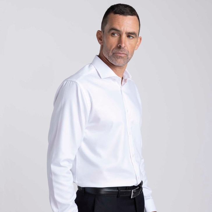 A white button-up shirt on a male model, featuring a collar and a logo. The model wears black trousers.