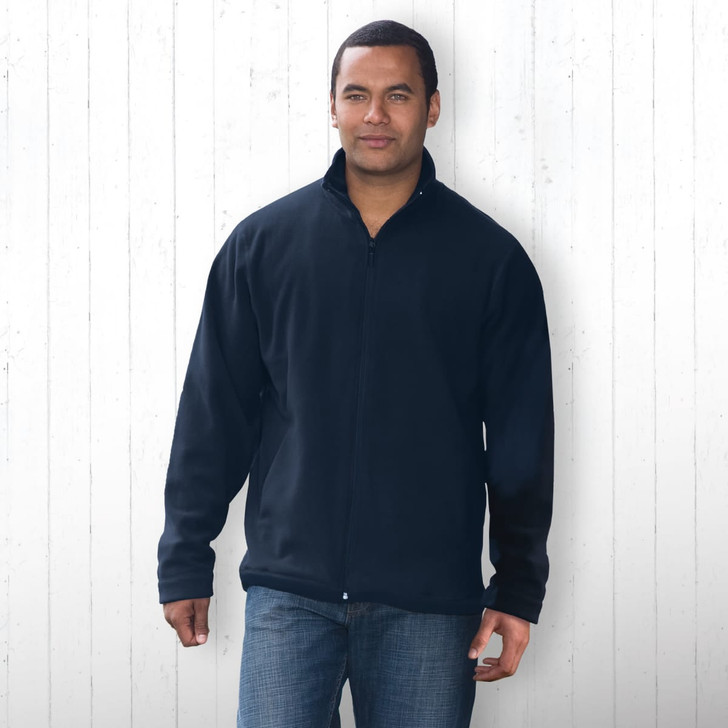 A man wearing a navy polar fleece jacket, featuring a zip front and a casual fit, stands against a white wooden backdrop.