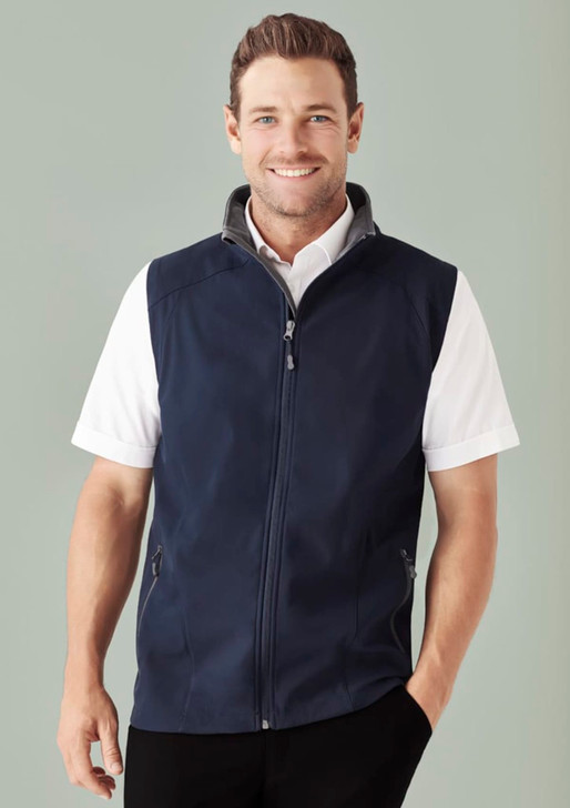 A man wearing a navy blue vest over a white shirt, displaying a stylish design with a logo on the chest.