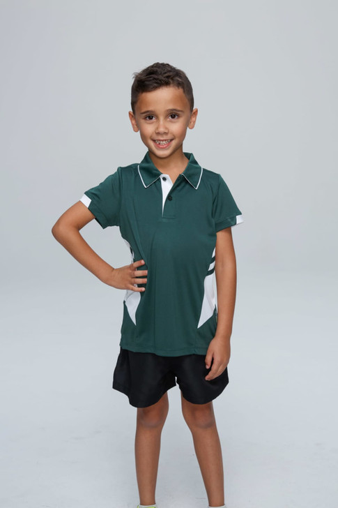 A young boy wearing a green and white polo shirt with black shorts, smiling while posing with one hand on his hip.