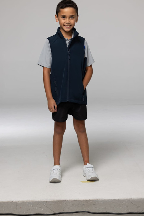 A child models a navy blue vest with a zip, paired with a grey shirt and black shorts. The vest features a logo.