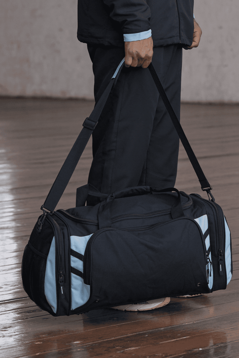 A black duffle bag with light blue accents, featuring multiple zippered pockets and a shoulder strap.