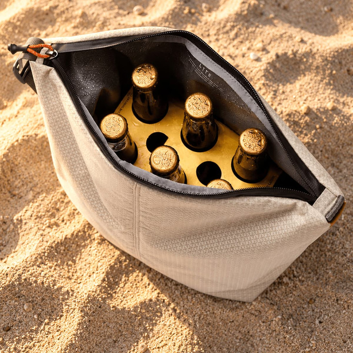 A cooler bag in light grey containing six dark bottles, set against a sandy background.