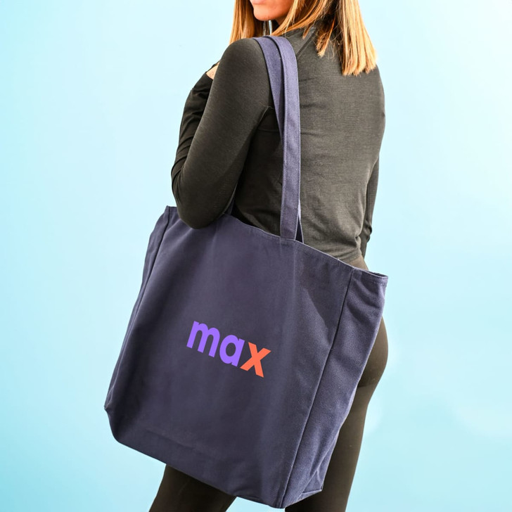 A navy blue tote bag with a logo on the side, being carried by a person from behind.