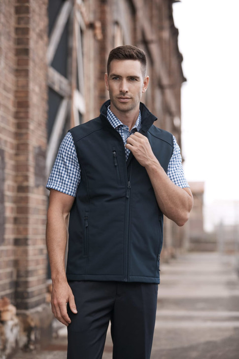 A men's black vest is featured, designed for workwear, with a zip closure and a logo. The model is posing outdoors.